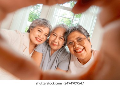 Group of Happy Asian senior mature women relaxing on sofa in living room. Elderly retired woman friends enjoy and fun reunion meeting using mobile phone taking selfie or vlogging together at home. - Powered by Shutterstock