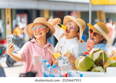 Group of Happy Asian senior woman enjoy travel in the city on summer holiday vacation. Elderly women friends using smartphone taking selfie during travel street market and eating street food together. - Powered by Shutterstock