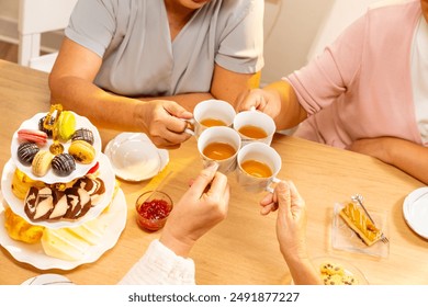 Group of Happy Asian senior women friends having afternoon tea together at home. Elderly retired woman enjoy and fun indoor lifestyle talking together with drinking tea and eating bakery on the table. - Powered by Shutterstock