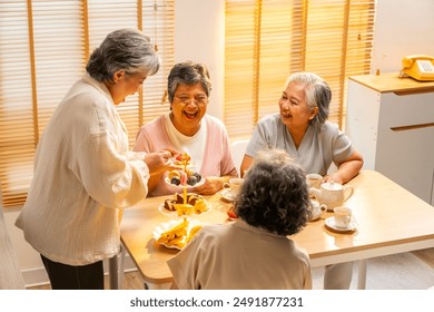 Group of Happy Asian senior women friends having afternoon tea together at home. Elderly retired woman enjoy and fun indoor lifestyle talking together with drinking tea and eating bakery on the table. - Powered by Shutterstock