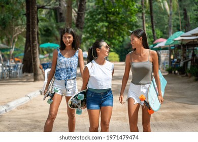 Group Of Happy Asian Woman Girl Friends Carry Skateboard Walking With Talking Together By The Beach. Female Friendship Enjoy Summer Outdoor Activity Lifestyle Play Extreme Sport Surf Skate Together