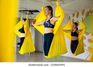 Group of happy athletic woman practicing fly aero yoga Iyengar hanged in high, low and medium yellow hammock. Smiling sports female performing asana turning shoulders at yogi gym studio