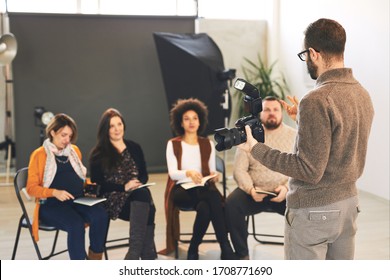 Group of happy attendees sitting and listening their tutor who holding camera and explaining them basics. - Powered by Shutterstock