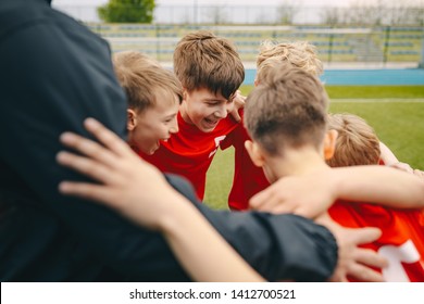 Group Of Happy Boys Making Sports Huddle. Smiling Kids Standing Together With Coach On Grass Sports Field. Boys Talking With Coach Before The Football Game. Happy Children Making Sport