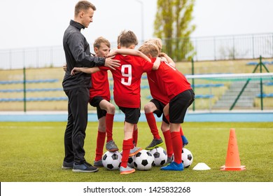 Group Of Happy Boys Making Sports Huddle. Smiling Kids Standing Together With Coach On Grass Sports Field. Boys Talking With Coach Before The Football Game. Happy Children Making Sport