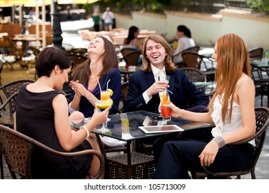 Group of happy business partners or friends enjoy colorful cocktails and talk outdoors. They use tablet and smart phones.
