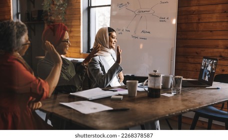 Group of happy businesswomen waving their hands during an online meeting in a modern office. Multicultural businesswomen having a video conference with their business partners in a creative workplace. - Powered by Shutterstock