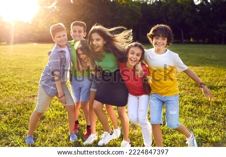 Group of happy cheerful active little children enjoying summer break, meeting in park, frolicking on green grass, playing fun games, making new friends, hugging, smiling and having great time together