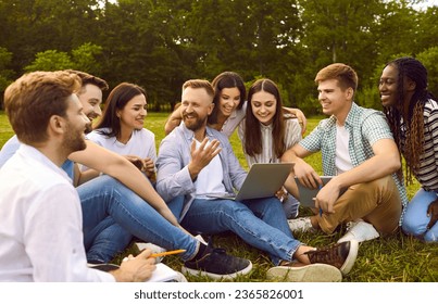 Group of happy, cheerful, diverse, multiethnic student friends sitting on green grass outside, studying information for project together, discussing something, using online tools on modern laptop PC - Powered by Shutterstock