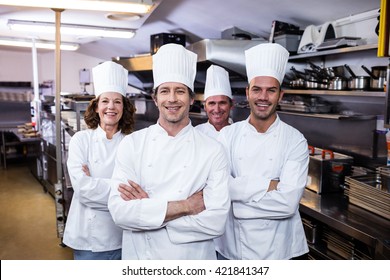 Group of happy chefs smiling at the camera in a kitchen wearing uniforms - Powered by Shutterstock