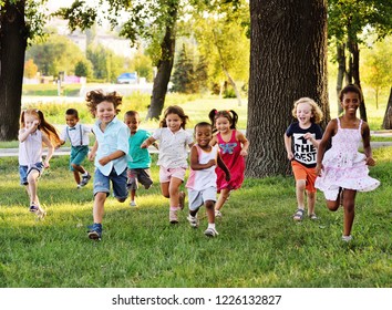 A group of happy children of boys and girls run in the Park on the grass on a Sunny summer day . The concept of ethnic friendship, peace, kindness, childhood.