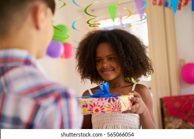 Group Of Happy Children Celebrating Birthday At Home, Kids Having Fun At Party. Cute Black Girl Giving Gift Box To Friend.