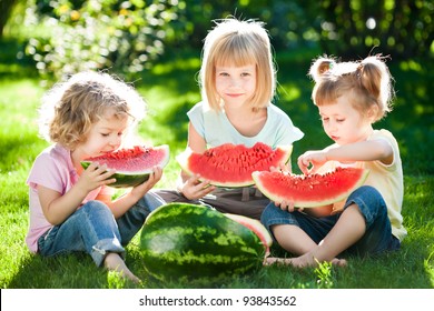 Group Of Happy Children Eating Watermelon Outdoors In Spring Park