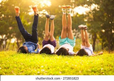 Group Of Happy Children Lying On Green Grass Outdoors In Spring Park