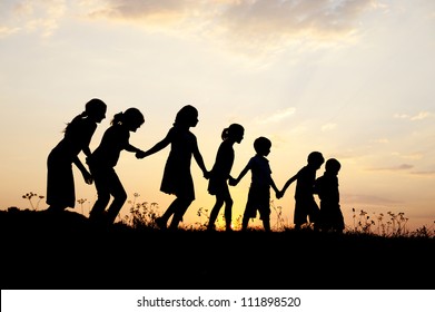 Group of happy children playing on meadow at sunset