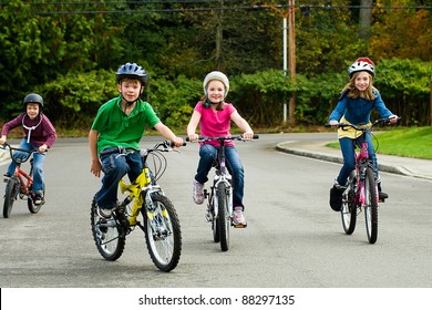 A group of happy children safely riding their bicycle on the street while wearing a helmet.