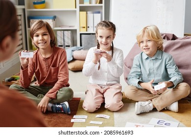 Group of happy children sitting on the floor and playing in English game together with teacher in the classroom