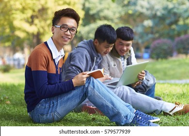 Group Of Happy Chinese College Students  Reading Book On Lawn In Campus