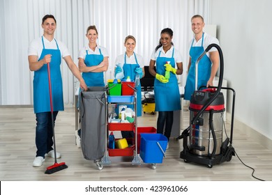 Group Of Happy Cleaners Standing With Cleaning Equipments In Office