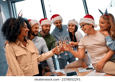 A group of  happy colleagues in Santa Claus hats celebrate the New Year at work in the office, drinking champagne. - Powered by Shutterstock