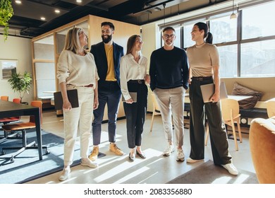 Group of happy colleagues smiling cheerfully while standing in an office. Team of successful businesspeople standing together in a creative and modern workplace. - Powered by Shutterstock