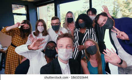 Group of happy diverse business colleagues posing, waving for selfie photo in masks against COVID-19 at modern office.