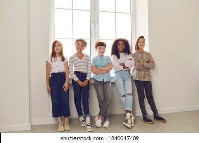 Group Of Happy Diverse Friends Standing By The Window, Looking At Camera And Smiling In New Home Or During Break At School Or Educational Center. Children's Development, Intercultural Kids Community