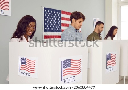 Group of happy diverse multiracial American citizens voting at polling station during democratic presidential elections. Several people standing in booths with USA flags and marking votes on ballots