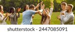 Group of happy diverse people celebrate victory in outdoor team game in green summer park. Joyful young man and woman give each other high five while their friends clap hands and cheer