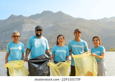 group of happy diverse volunteers enjoy charitable working together to clean up river beach by picking trash into garbage bags for recycling and separating reused plastic for waste management - Powered by Shutterstock