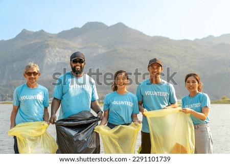 group of happy diverse volunteers enjoy charitable working together to clean up river beach by picking trash into garbage bags for recycling and separating reused plastic for waste management