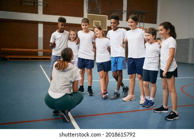 Group Of Happy Elementary Students With Physical Education Teacher During A Class At School Gym. 