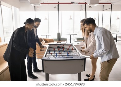 Group of happy engaged multiethnic colleagues playing toy football, fighting in table soccer, having fun, enjoying office leisure environment, work break activity, laughing at board game - Powered by Shutterstock