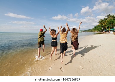 Gruppe glücklicher aufgeregter junger Menschen, die Waffen anziehen und am Strand laufen