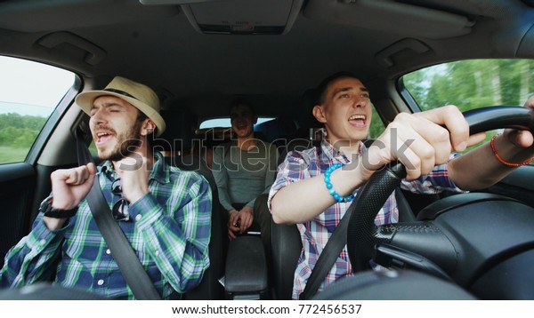 Group of happy friends in car singing and dancing\
while drive road trip