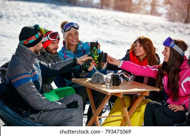 Group Of Happy Friends Cheering With Drink After Skiing Day In Cafe At Ski Resort