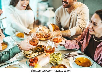 Group of happy friends clinking rose wine glasses - Smiling young people enjoying dinner party at home - Life style concept with guys and girls eating meal and drinking alcohol - Focus on left glass - Powered by Shutterstock