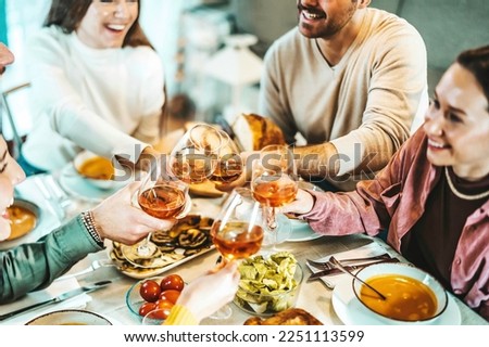 Group of happy friends clinking rose wine glasses - Smiling young people enjoying dinner party at home - Life style concept with guys and girls eating meal and drinking alcohol - Focus on left glass