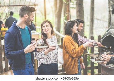 Group Of Happy Friends Cooking And Eating At Barbecue Dinner Outdoor - Young People Toasting Wine For Bbq In Wood House Backyard - Friendship Concept - Focus On Left Man Face