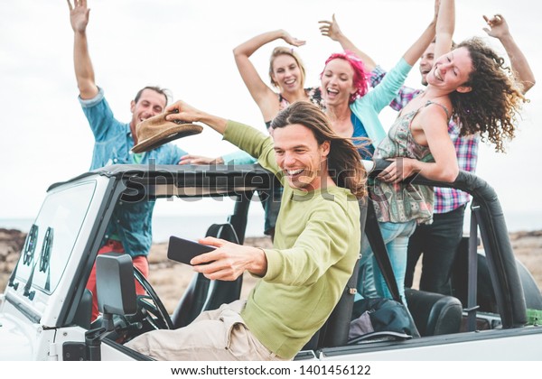 Group of happy friends doing excursion on desert\
in convertible 4x4 car - Young people having fun traveling together\
- Friendship, tour, youth and vacation concept - Focus on man\
taking selfie