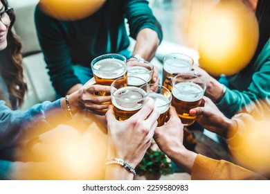Group of happy friends drinking and toasting beer glasses at brewery pub restaurant - Young people enjoying happy hour sitting at bar table - Food, beverage and life style concept