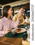 Group of happy friends eating lunch together in a restaurant. They eat delicious salads, hamburgers, bread and meat.