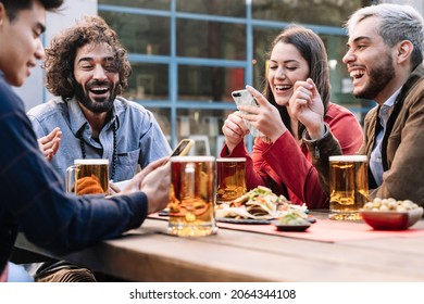 Group of happy friends enjoying a beer and food in outdoors bar pub in the afternoon after work, sharing good moments in social media with smart phones - Powered by Shutterstock