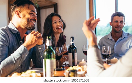 Group of happy friends enjoying party at home. Men and women sitting at dining table and enjoying meal together.