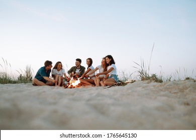 Group of happy friends frying sausages on campfire at the beach. A company of young people came together for a barbecue.
 - Powered by Shutterstock