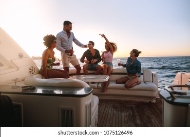 Group of happy friends having a boat party. Diverse men and women having drinks at sunset yacht party and dancing.