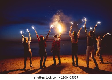 Group of happy friends is having fun or celebrating something with signal fires at evening beach