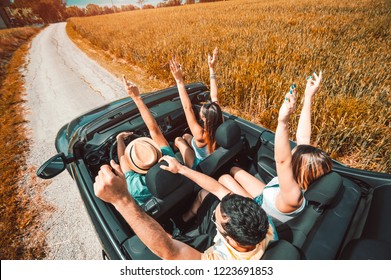 Group Of Happy Friends Having Fun With Hands Up On A Convertible Car At Roadtrip. Concept About Transport, Rental Cars, People And Lifestyle