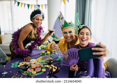 Group Of Happy Friends Having Fun While Photo Messaging With Smart Phone During Mardi Gras Party At Home. 