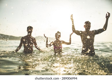 Group Of Happy Friends Jumping In To Water At Sunset - Silhouettes Of Active People Dancing And Having Fun On The Beach On Vacation